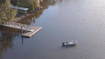 Aerial footage captures a small boat on a calm river near a dock, surrounded by lush greenery under soft lighting video
