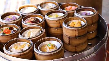 Hands selecting steamed dim sum from bamboo baskets in a vibrant Phuket market. Bright lighting highlights the colorful variety video