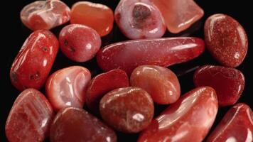 Red jasper stones rotate smoothly against a black backdrop, highlighting their rich colors and polished surfaces under soft lighting video