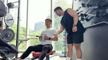 A trainer guides a client through a seated cable row exercise in a well-lit gym setting video