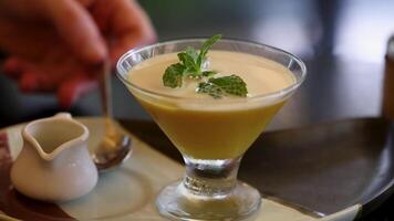 A spoon dips into a creamy mango custard garnished with mint, highlighting a delightful dessert experience video