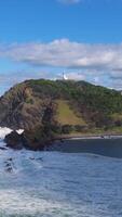 Aerial view of Byron Bay lighthouse on a sunny day with ocean waves crashing against the rocky shore video