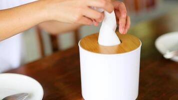 A hand pulls a tissue from a stylish dispenser on a wooden table in a well-lit dining setting video