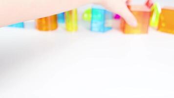 Hands manipulate colorful transparent cubes on a white surface, illustrating geometric concepts with vibrant lighting and clear focus video