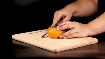 Hands slicing persimmon on a wooden board video