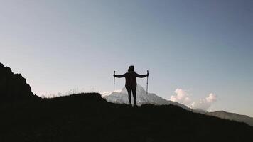 Silhouette of woman with arms raised outstretched and trekking poles in hand facing Mount Kazbek, celebrating mountain summit sunrise in Georgian Caucasus mountains range. Kabarjina viewpoint panorama video