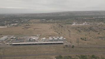 Aerial view of industrial fuel storage tanks, freight train, warehouses, and pipelines in arid landscape with distant hills and power lines video