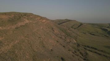 Aerial view serene rolling green hills with winding paths under soft warm sunset light. video