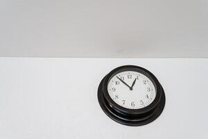 On a clean, white wall, there is a striking black clock beautifully hanging. This clock serves as a functional timepiece while also adding an artistic element to the decor photo