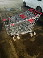 An empty shopping cart is parked next to a sleek white car in a busy parking lot, creating an unusual and intriguing scene amidst the diverse array of vehicles surrounding it photo