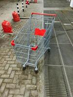 On a bright and sunny day, a shopping cart featuring a striking red handle is parked neatly on the sidewalk, patiently waiting to be picked up and used by nearby potential shoppers photo
