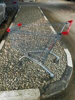 A shopping cart, made from materials such as steel and aluminum, is sitting idle on the side of the road, possibly abandoned or left behind for someone to pick up and use photo