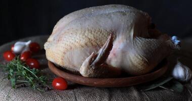 Whole chicken surrounded by fresh herbs and vegetables on a wooden plate photo