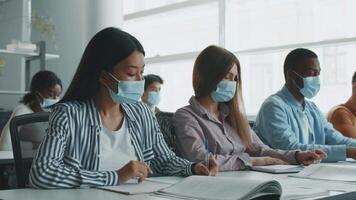 Diverse college students are focused on their studies, wearing masks while taking notes and collaborating in an interactive classroom environment, showcasing a commitment to education. video