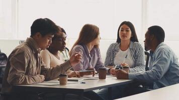 A group of diverse students engages in a collaborative study session at a university. They are discussing ideas and taking notes while seated around a table filled with notebooks and drinks. video