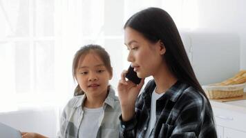 Mother and daughter share a warm moment in the kitchen, with the mother on the phone and the girl attentively watching. They create a loving atmosphere during their time together at home. video