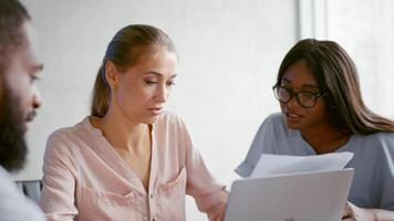 Three professionals engage in a productive meeting in a bright office. One person reviews documents while another contributes ideas, fostering collaboration and strategic planning. video