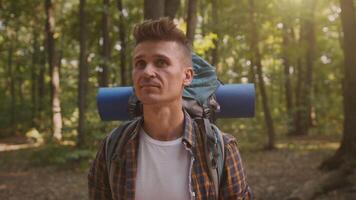 A hiker stands in a lush green forest, ready for a camping trip. The sun filters through the trees, illuminating his focused expression while he prepares to embark on the trail, fully equipped. video