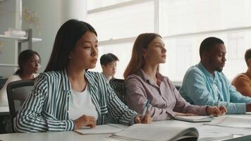 Diverse group of college students is focused on their studies in a bright university classroom. They are taking notes and participating in a learning environment that fosters collaboration. video