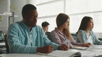 In a modern university classroom, diverse students actively participate in study sessions. They take notes and collaborate on academic assignments while surrounded by natural light. video