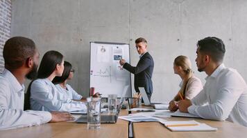 A focused team meets in a contemporary office to discuss project strategies. The presenter highlights key data on a whiteboard while team members engage and take notes. video