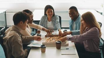 Groups of diverse students gather around a table in a bright university study space, enjoying pizza and coffee while engaging in lively discussions and collaboration on class projects. video