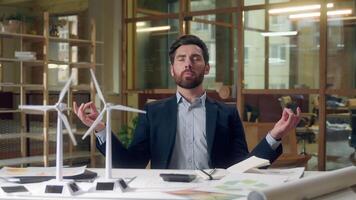 Engineer meditating business wind turbine project models stress relief green startup renewable energy design focus Caucasian man male peaceful businessman mindfulness sustainable innovation at office video