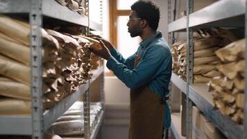 Focused thoughtful African American coffee warehouse worker man guy male inspecting stacked coffee packages quality control process look shelves checking caffeine package storage precision evaluation video