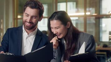 Multiethnic happy businesspeople coworkers discuss reports documents at office Caucasian businessman Korean businesswoman partners managers laughing success finance startup showing clipboard talking video