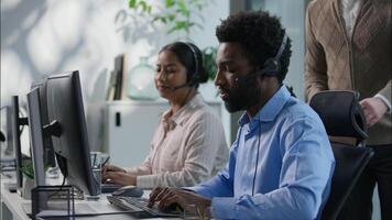 Callcenter teamwork multicultural office operators support communication African man Indian woman headset computer helpdesk Caucasian supervisor pointing monitor giving instructions customer service video