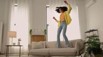 Funny African American woman happy girl at home dancing jumping have fun fooling joy testing comfortable soft couch cozy sofa furniture for apartment dance to music jump rejoice moving day relocation video