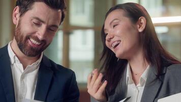 Multiracial laughing Korean Caucasian colleagues joke discussing paperwork report charts business documents woman man communication joy teamwork cooperation indoors success office unity confidence video