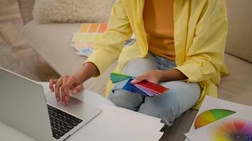 Unrecognizable woman businesswoman graphic designer architect hold multicolored palette catalog samples of rainbow colors wall paint choose color new interior design house renovation working on laptop video