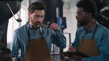 Two diverse coffee factory workers examine aroma test document roasting results African American barista write checklist Caucasian colleague evaluates beans flavor precision espresso quality session video