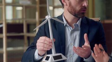 Ecology project business negotiation Caucasian businessman engineer holding hands windmill model turbine explaining Korean woman green tech investor speaking mechanism environment nature energy office video