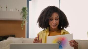 African American business woman designer talk online call on computer laptop discuss home design show sample colors presentation smiling businesswoman help client choose paint color on papers video