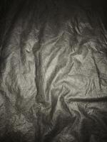 Wrinkled black synthetic fabric with subtle lighting and visible surface texture, ideal for background use in fashion, product display, or design elements that need dark textile feel. photo