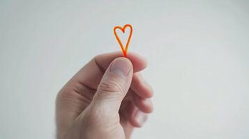 Hand holding a small orange heart shape made of thread against a neutral background symbolizing love and creativity photo