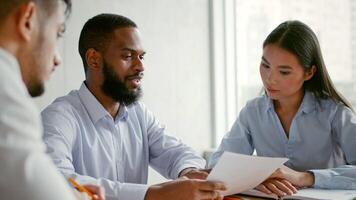 Three professionals engage in a brainstorming session at a sleek office. They examine important documents while sharing insights and ideas that drive business success in the competitive market. video