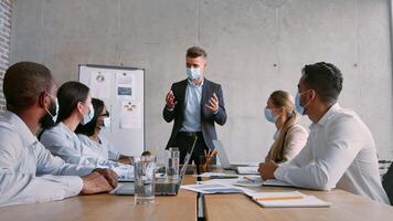 A group of professionals engages in a productive discussion about success strategies. They are wearing masks and seated around a table filled with documents and laptops in a contemporary office. video