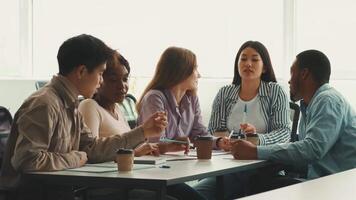 A group of diverse students engages in collaborative study at a university. They share ideas, taking notes and discussing while seated at a table with coffee cups. video