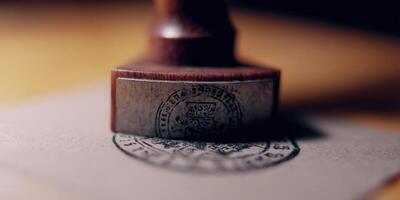 A wooden stamp presses down on paper, creating an official and detailed seal against a warm backdrop. photo
