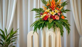 close up view of a podium wrapped in ivory cloth and topped with a tall arrangement of mixed tropical flowers and large green leaves. photo