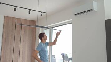 Man using remote control to adjust temperature on wall-mounted air conditioner in modern home interior. Concept of home cooling and indoor climate control during hot summer weather video