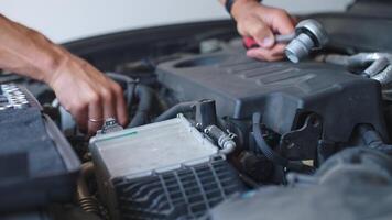 Close-up view of mechanic using ratchet tool to repair car engine under open hood. Auto service, car maintenance and technical repair video