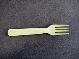 Yellow plastic fork on dark textured surface photo