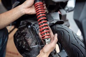 Motorcycle mechanic check and change rear Shock Absorbers motorcycle at motorcycle garage, Damaged Struts and fluid leaks among struts and shocks ,repair, maintenance and service concept photo