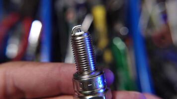 A detailed close-up image featuring a hand holding a clean spark plug against a blurred background of mechanical tools and equipment. video