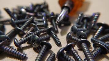 Close-Up of screws and screwdriver on a wooden surface. Pile of steel chrome screws rotating on isolated background video