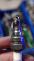 A hand holding a used spark plug, showcasing signs of wear and carbon buildup from engine use. video